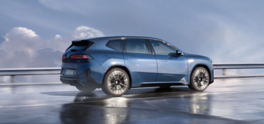 La BMW iX3 in colore blu &egrave; ai margini di una spiaggia atlantica con sfondo del cielo azzurro e nuvole.