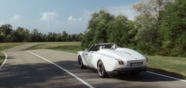 La Rolls-Royce Project Nightingale in fase di test su strada. La vettura &egrave; di colore bianco e la strada &egrave; in aperta campagna con del verde nei dintorni.