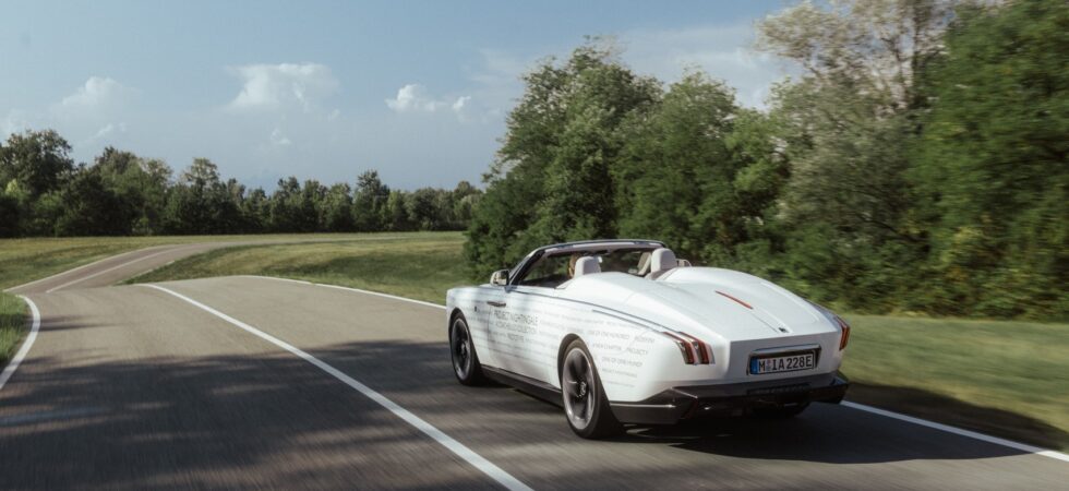La Rolls-Royce Project Nightingale in fase di test su strada. La vettura &egrave; di colore bianco e la strada &egrave; in aperta campagna con del verde nei dintorni.